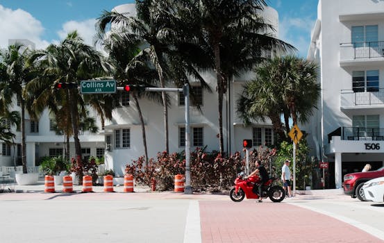 Motorcycle passing Collins Avenue in sunny Miami Beach, with palm trees and art deco architecture.